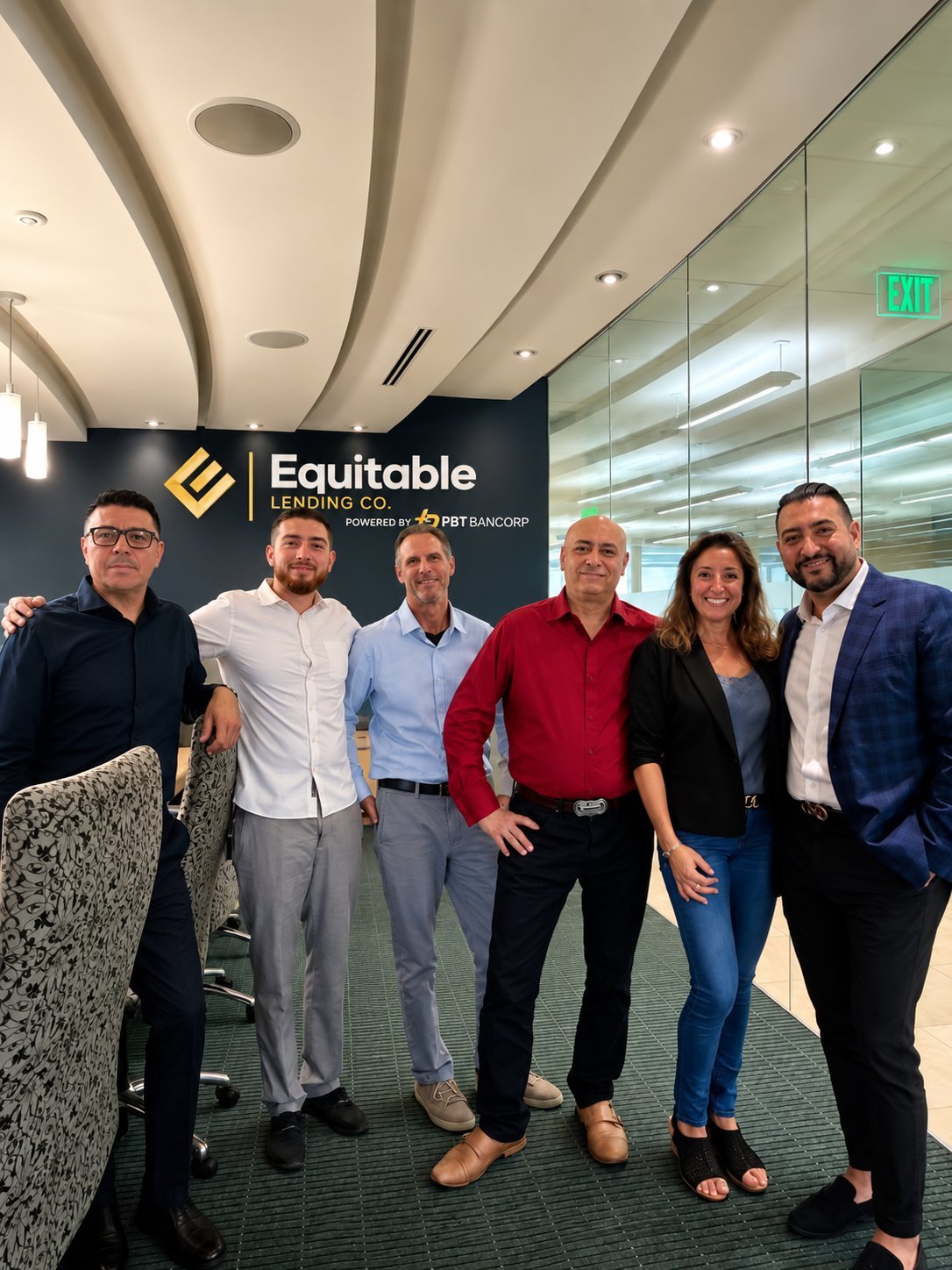 Six professional staff members standing together in front of Equitable Lending Co. office sign with glass walls and green exit sign visible