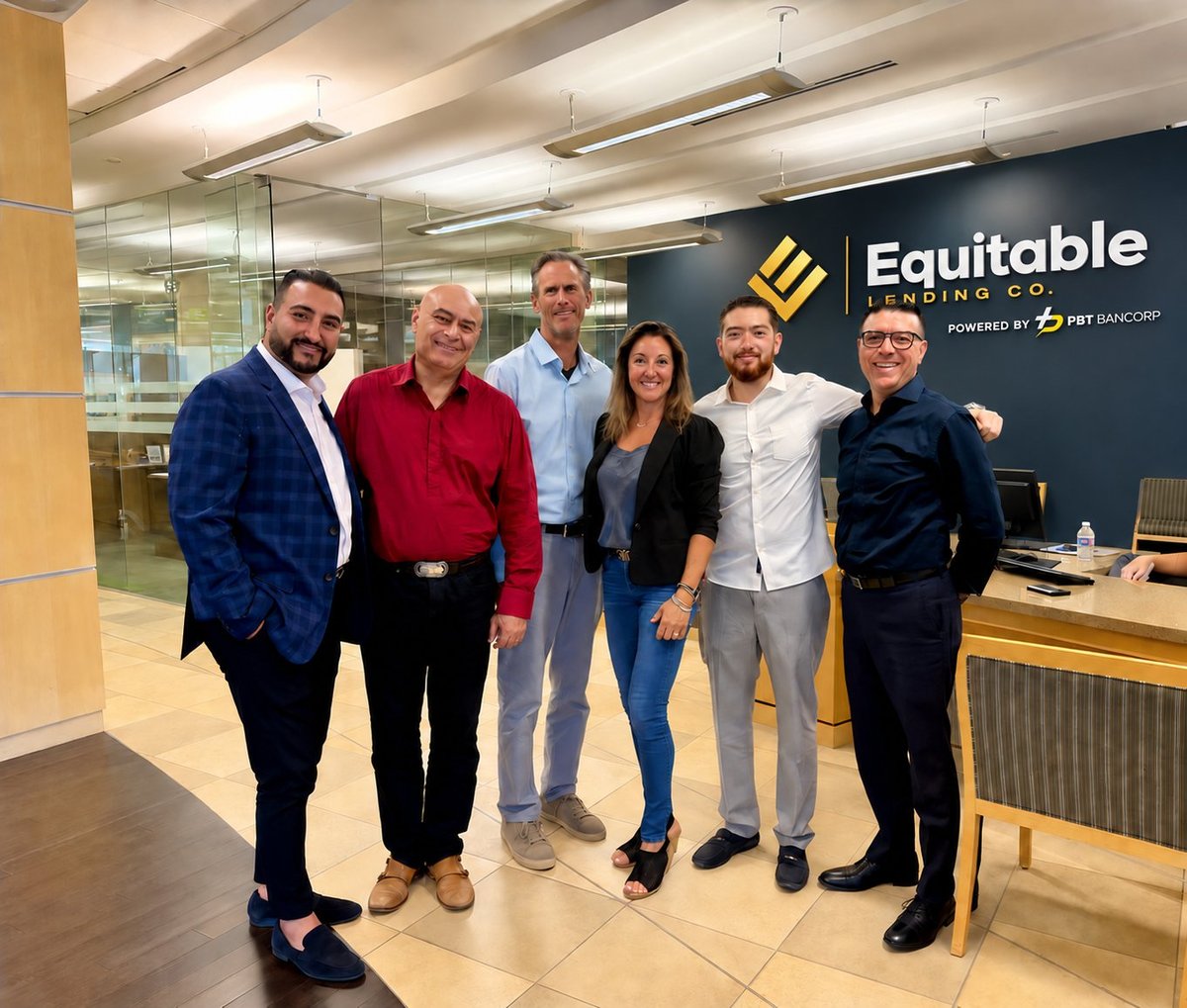 Six business professionals posing together in an office lobby with Equitable Holding Company signage visible on the wall behind them